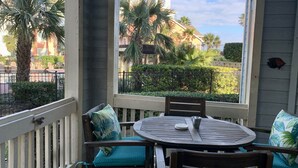 A balcony with a round table and chairs, a view of a building with palm trees, and a fence. - <br>The Dolphin Poolside at The Dawn. (Galveston)