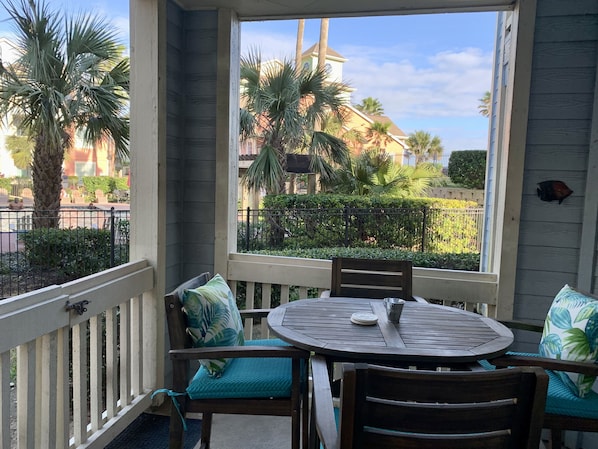 A balcony with a round table and chairs, a view of a building with palm trees, and a fence.