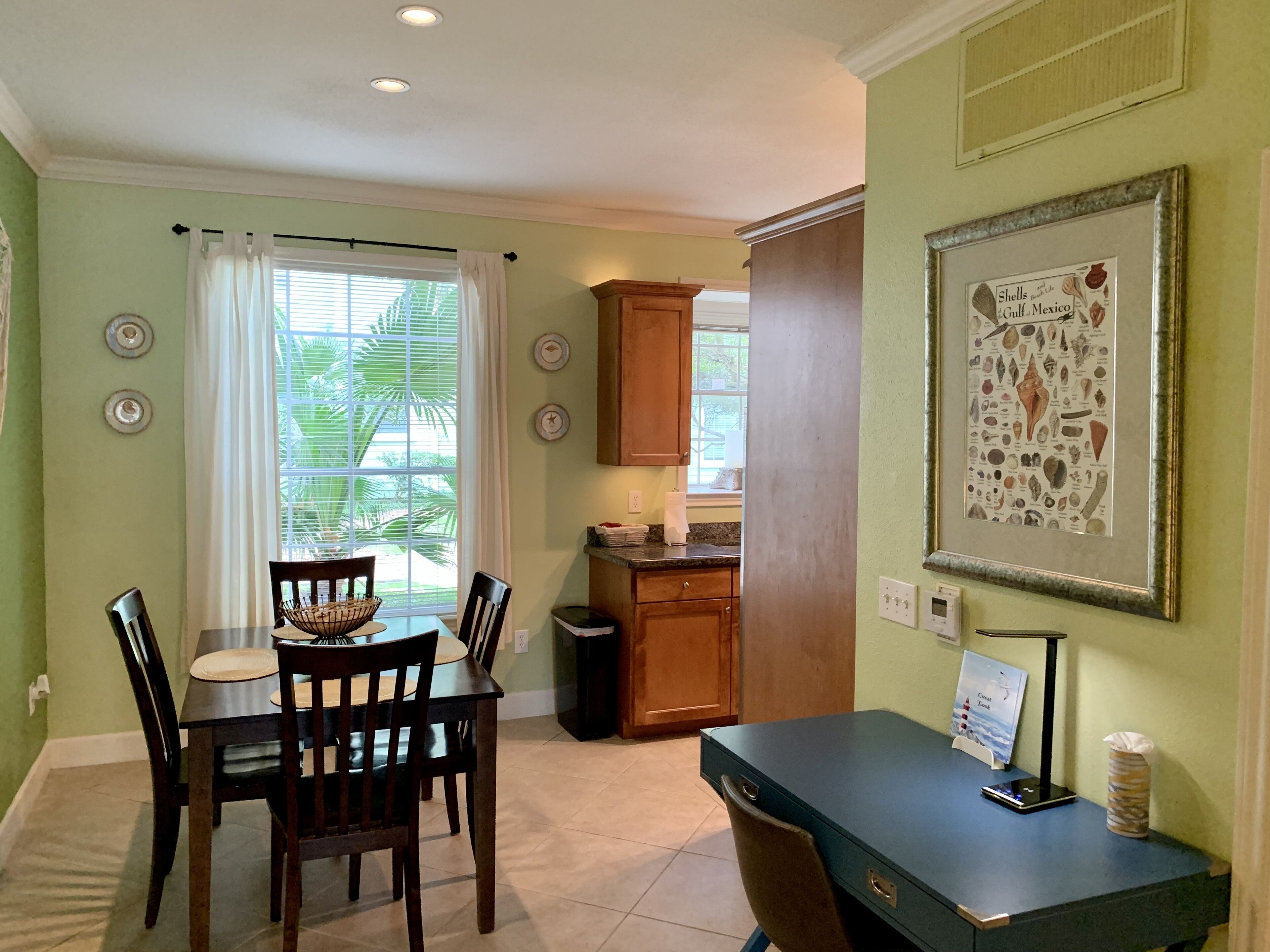 A dining area with a table and chairs, a kitchen area with cabinets, and a framed picture on the wall.