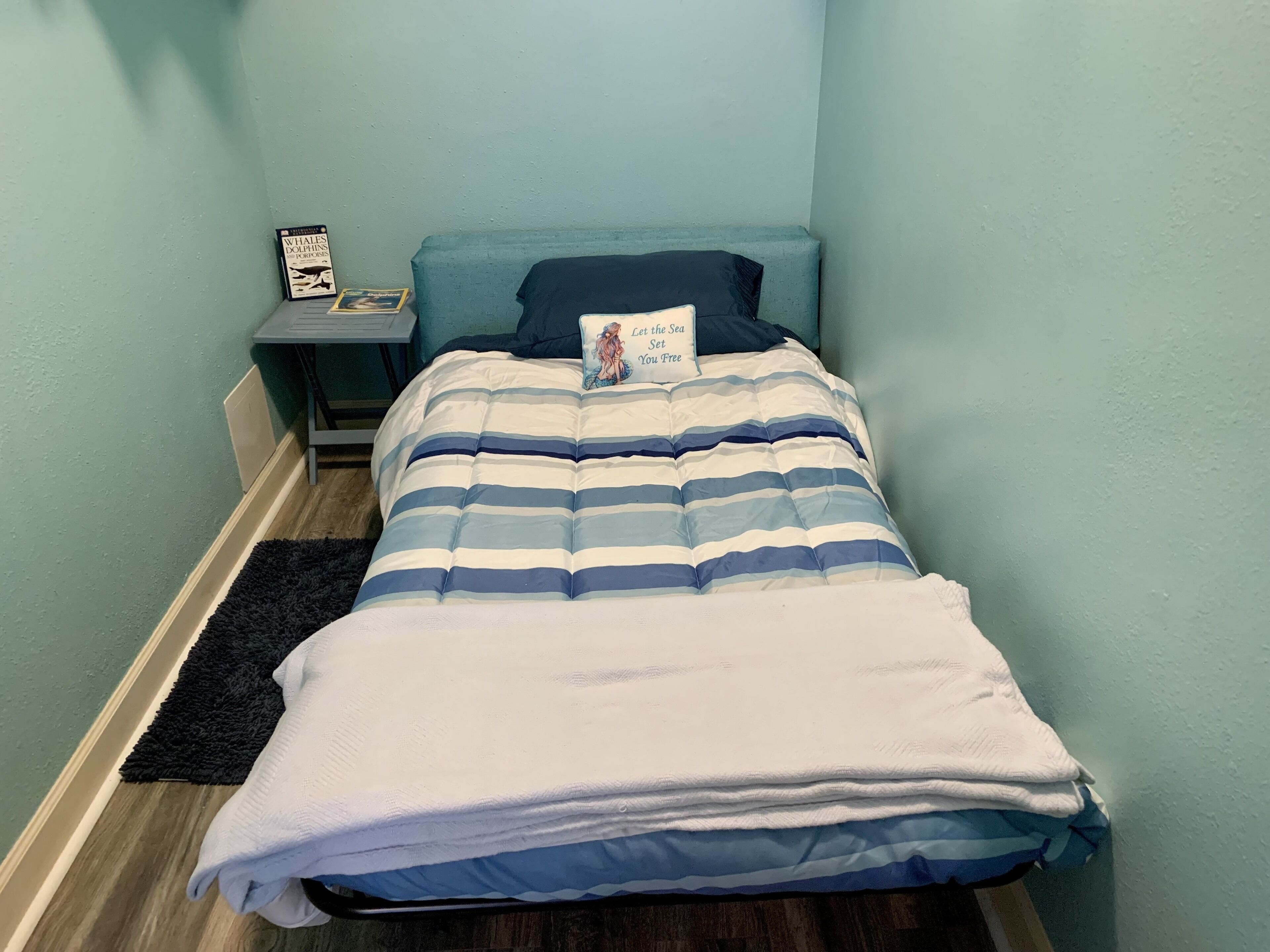 A neatly made bed with a striped bedspread and a pillow with a book cover.