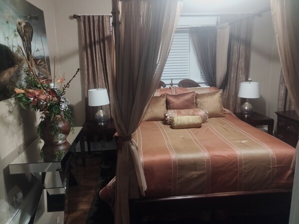 Une chambre à coucher avec un lit, deux tables de chevet avec des lampes, une table de nuit, un vase décoratif et des rideaux.