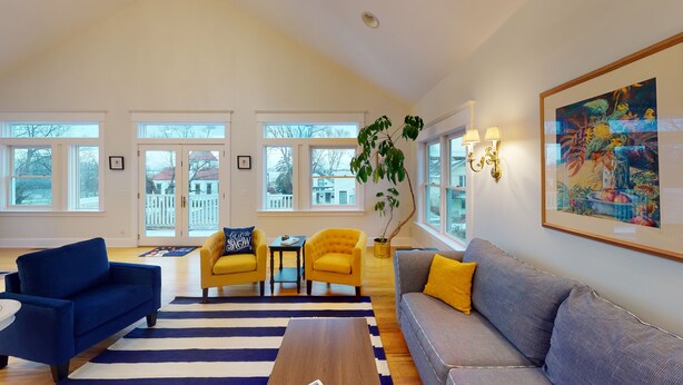 A spacious living room with a blue sofa, yellow armchairs, a grey sofa, and a striped rug. - Wonderful Main Street Location, next to the HS Historical Society! (Harbor Springs)