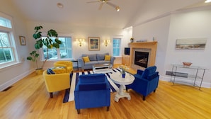 A spacious living room with a fireplace, a large window, and a ceiling fan. - Wonderful Main Street Location, next to the HS Historical Society! (Harbor Springs)