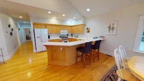 A modern kitchen with wooden cabinets, a central island, and a dining area with a round table and chairs. - Wonderful Main Street Location, next to the HS Historical Society! (Harbor Springs)