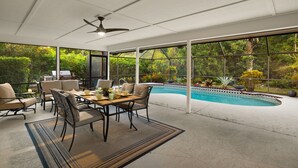 Un patio cubierto con piscina, mobiliario exterior y ventanas amplias que dan a la vegetación.