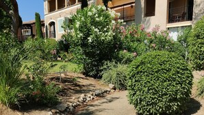 Um caminho que leva a um edifício com jardim, uma parede de pedra e um céu azul límpido.