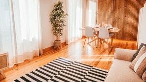 Una sala de estar moderna con piso de madera, un tapete a rayas, un sofá y un comedor con una mesa y sillas.