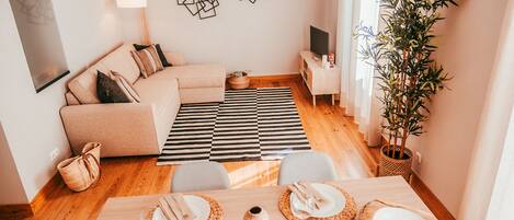 Una sala de estar moderna con un sofá, una mesa de comedor lista para cuatro personas, un televisor y una planta grande.