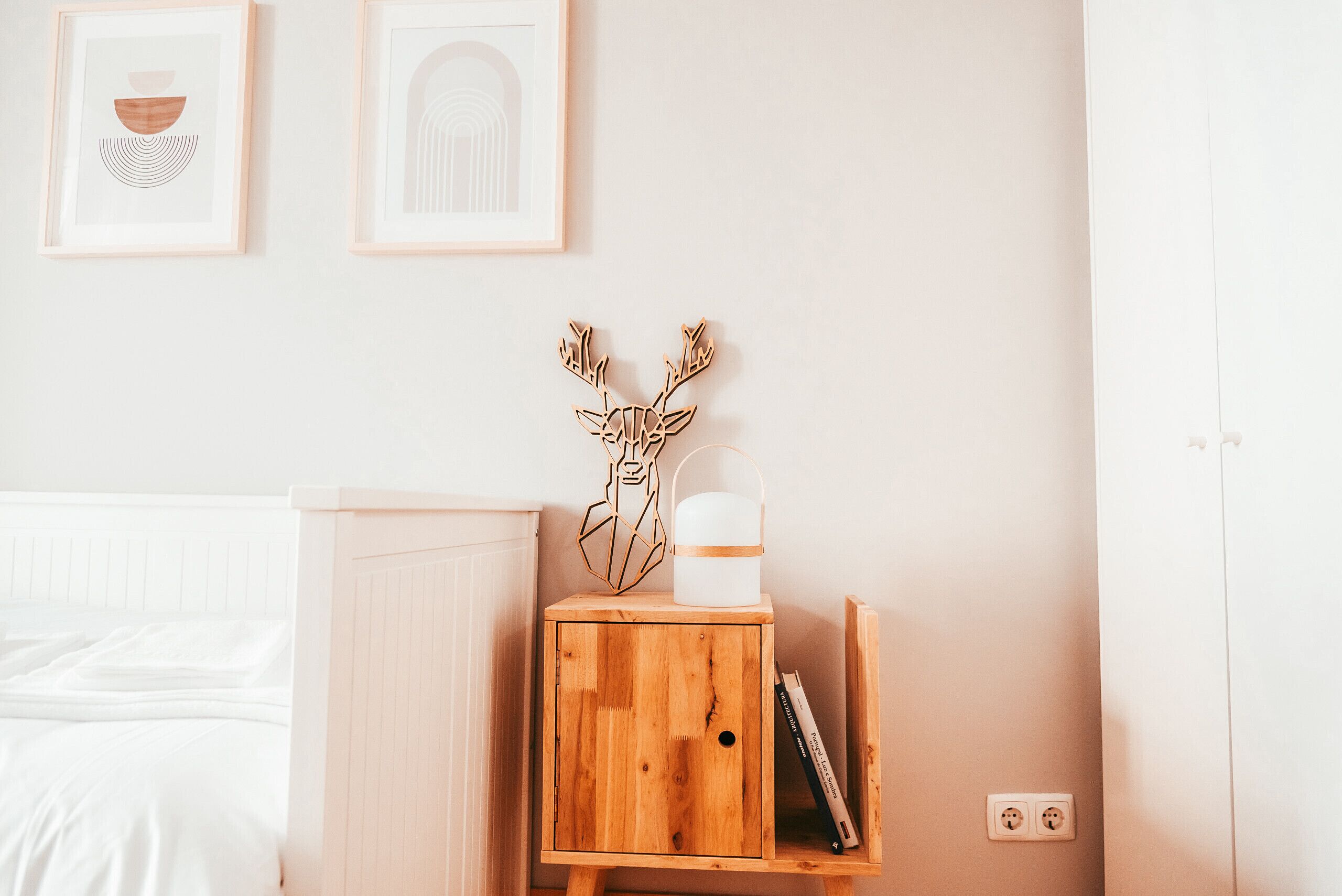 Een slaapkamer met een houten nachtkastje, een wit bed en twee ingelijste foto's aan de muur.