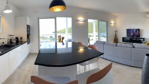 Una cocina moderna con una isla central, un comedor con mesa redonda y una sala de estar con sofá y televisor.