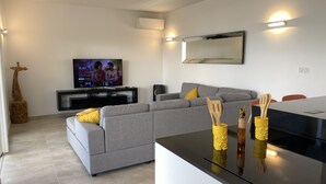 Una sala de estar moderna con un sofá gris, un televisor de pantalla plana y una zona de cocina con encimera negra.
