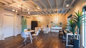 Un intérieur moderne avec un plancher en bois, des murs blancs et un plafond avec des poutres apparentes. On y trouve plusieurs tables et chaises disposées pour les repas ou les réunions.