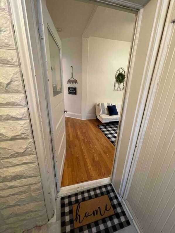 A hallway with a wooden floor leading to a room with a checkered doormat and a sign that reads "home".
