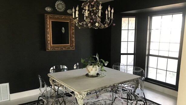 A dining room with a white table, clear chairs, a floral chandelier, and a large window.