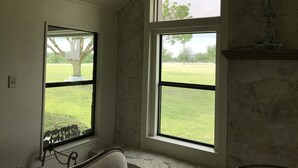 A room with two large windows, a stone fireplace, and a view of a grassy field.