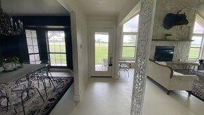 A spacious living room with a fireplace, a dining area with a chandelier, and large windows offering a view of the outdoors.