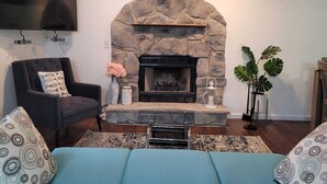 Una sala de estar con chimenea de piedra, un sillón negro, un sofá azul y un televisor de pantalla plana montado en la pared.