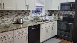 Una cocina moderna con armarios blancos, encimera de granito, lavavajillas, fregadero, microondas y horno.