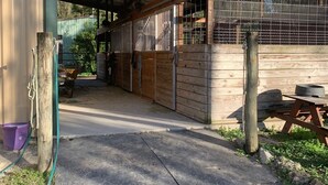 Un establo cubierto con paredes de madera y una reja metálica, un camino de acceso de hormigón y una mesa de picnic en el exterior.