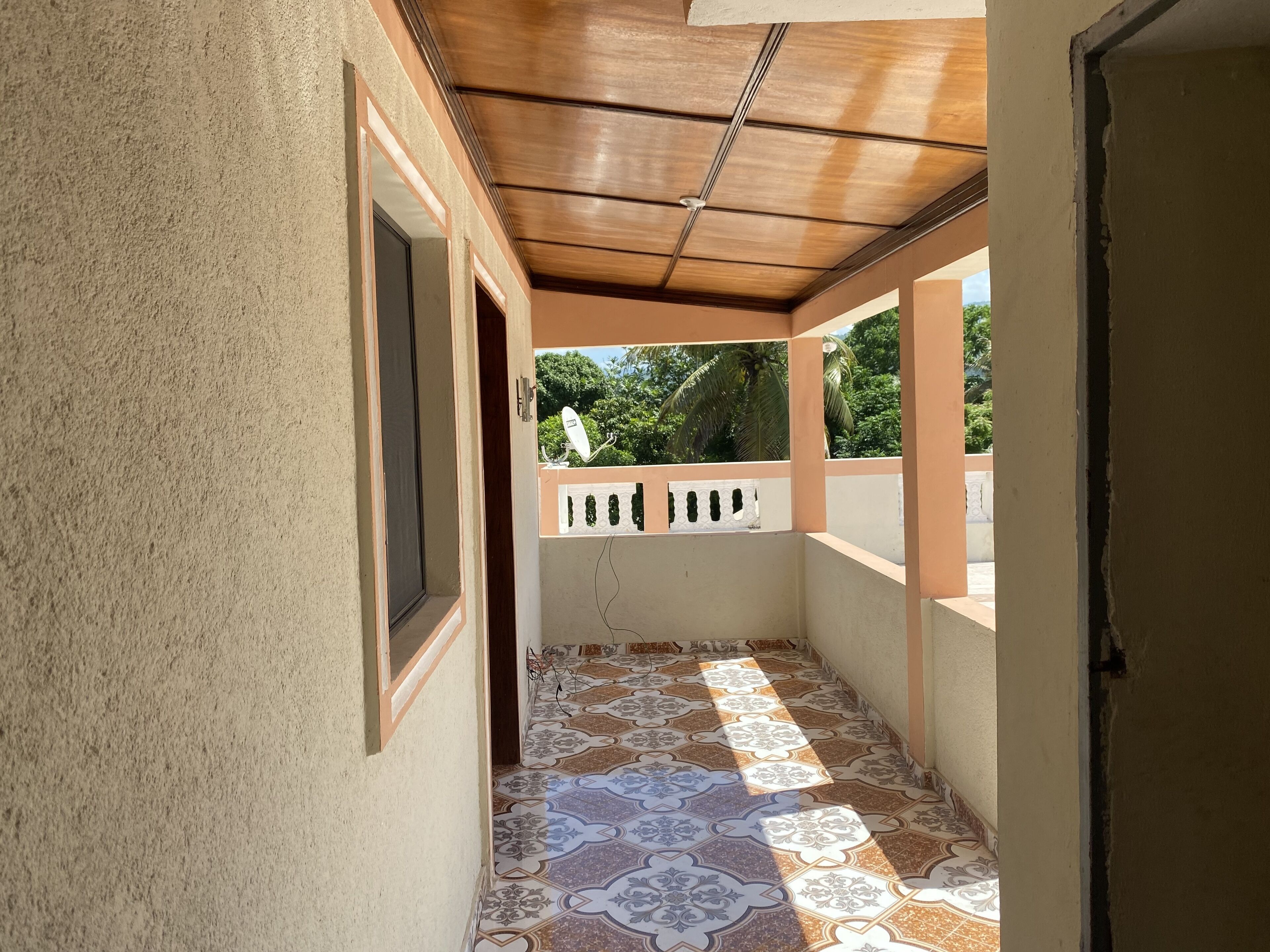 A corridor with patterned tiles, a wooden ceiling, and a view of greenery outside.
