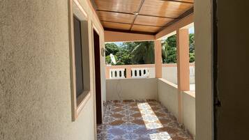 A corridor with patterned tiles, a wooden ceiling, and a view of greenery outside.