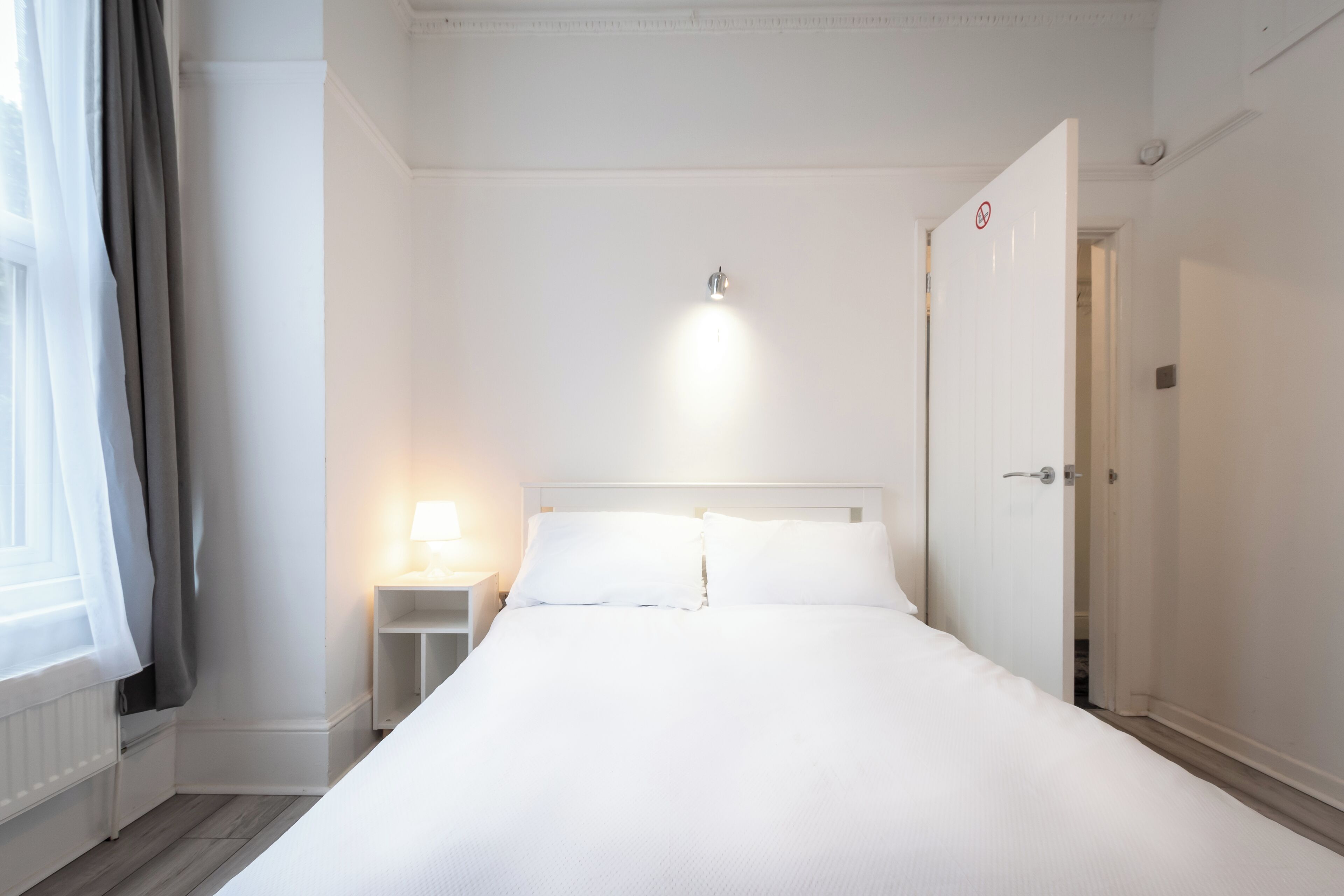 A neatly arranged hotel room with a large bed, a bedside table with a lamp, and a door with a 'no entry' sign.