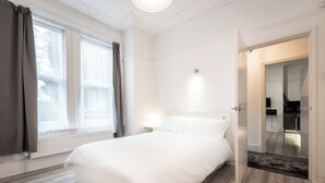 A bedroom with a large bed, a nightstand, and a door leading to a bathroom.