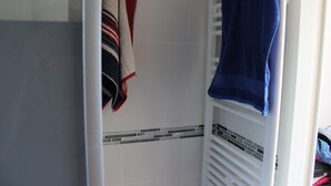 Un baño con ducha, un perchero y dos toallas, y piso de baldosas.