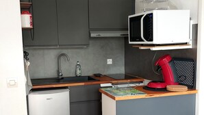 Cocina compacta con microondas, lavamanos y un reloj en la pared.