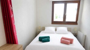 Un dormitorio con cama, dos lámparas de noche, una ventana y una mesita de noche de madera.