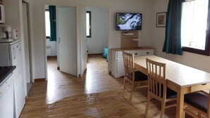 A compact kitchen with a microwave, coffee maker, and a small refrigerator. A wooden dining table with chairs is positioned near a window with curtains. - Lovely apartment in LUCHON, in a secure residence, wooded grounds (BAGNERES DE LUCHON)