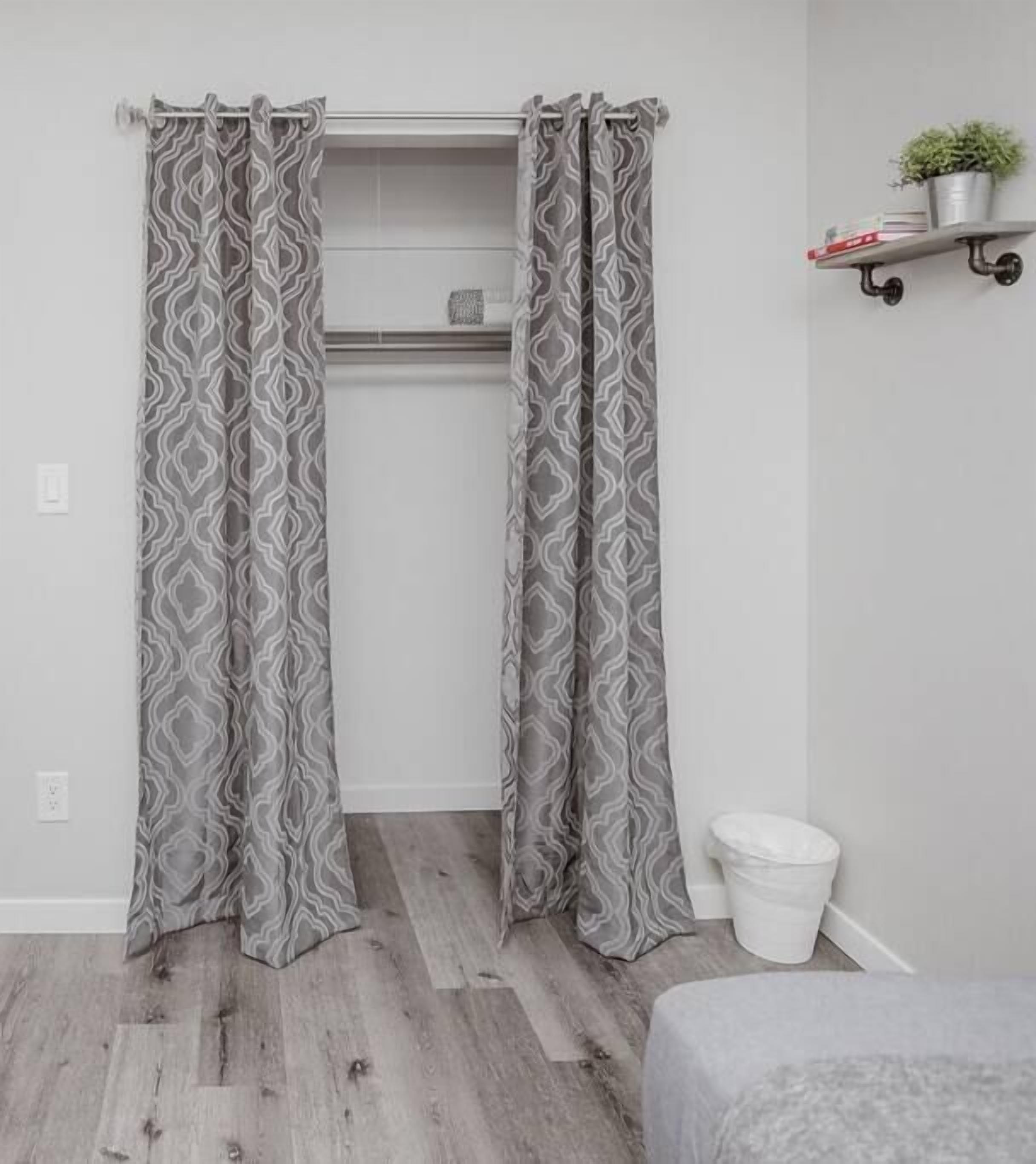 A bathroom with grey patterned curtains, a white toilet, and a small shelf with a plant.