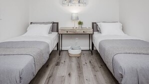 Kahden hengen huone, jossa on kaksi sänkyä, yöpöytä lampun kanssa ja seinälle ripustettu taideteos.