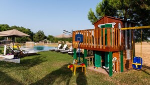 Un giardino sul retro con una casetta in legno, una piscina e sedie a sdraio.