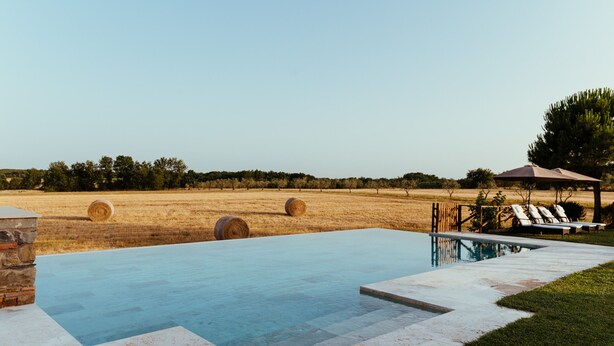 Una piscina con vista su un campo e balle di fieno.