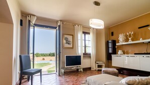 Una camera d'albergo con una grande finestra, una televisione a schermo piatto, un piccolo tavolo, un divano e un armadietto con oggetti decorativi.