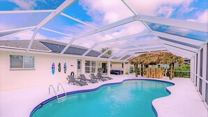 Una piscina interior con techo de vidrio, sillas de descanso y una estructura con techo de paja.
