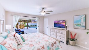 Un dormitorio con cama, televisión, ventilador de techo, puerta corrediza de vidrio a un patio y un cuadro en la pared.