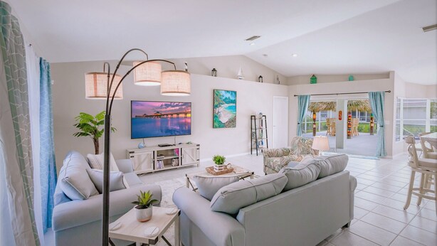 Una sala de estar moderna con sofá, mesa de centro y televisor, un comedor con sillas y vistas al exterior.