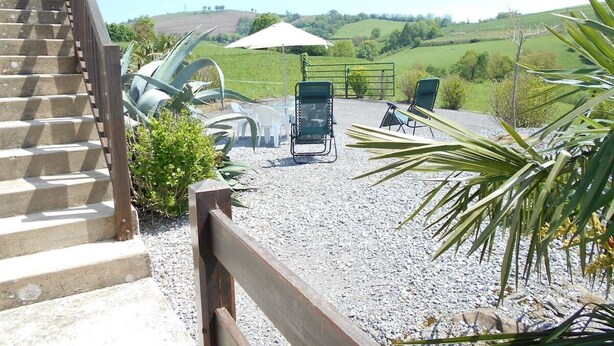 Een trap die leidt naar een patio met terrasmeubels en uitzicht op glooiende heuvels.