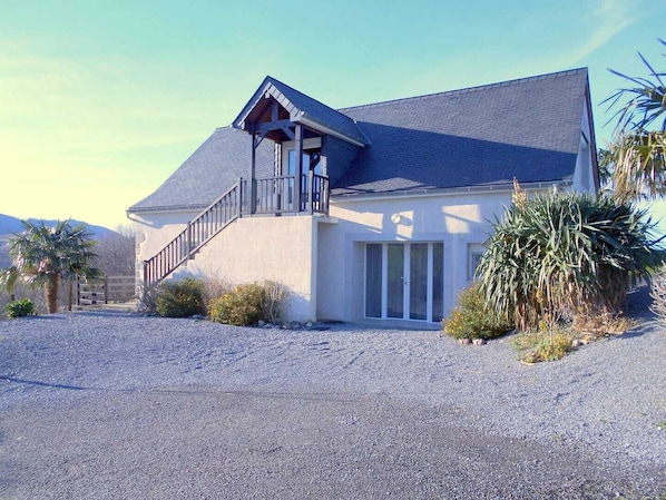 A two-story house with a balcony, a gravel driveway, and a palm tree in the foreground.