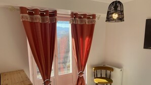 Een slaapkamer met een bed, een stoel, een radiator en gordijnen vastgebonden onderaan.