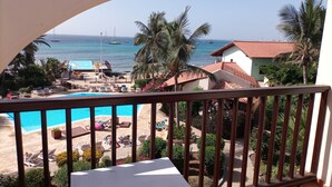 Un balcon avec vue sur une piscine, des chaises longues et une plage où sont amarrés des bateaux.