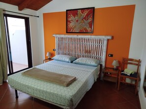 Une chambre à coucher avec un lit, une chaise, une table de chevet, une fenêtre et un tableau au mur.