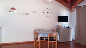 Un coin repas avec une table et des chaises en bois, une horloge murale blanche, un téléviseur et un meuble.
