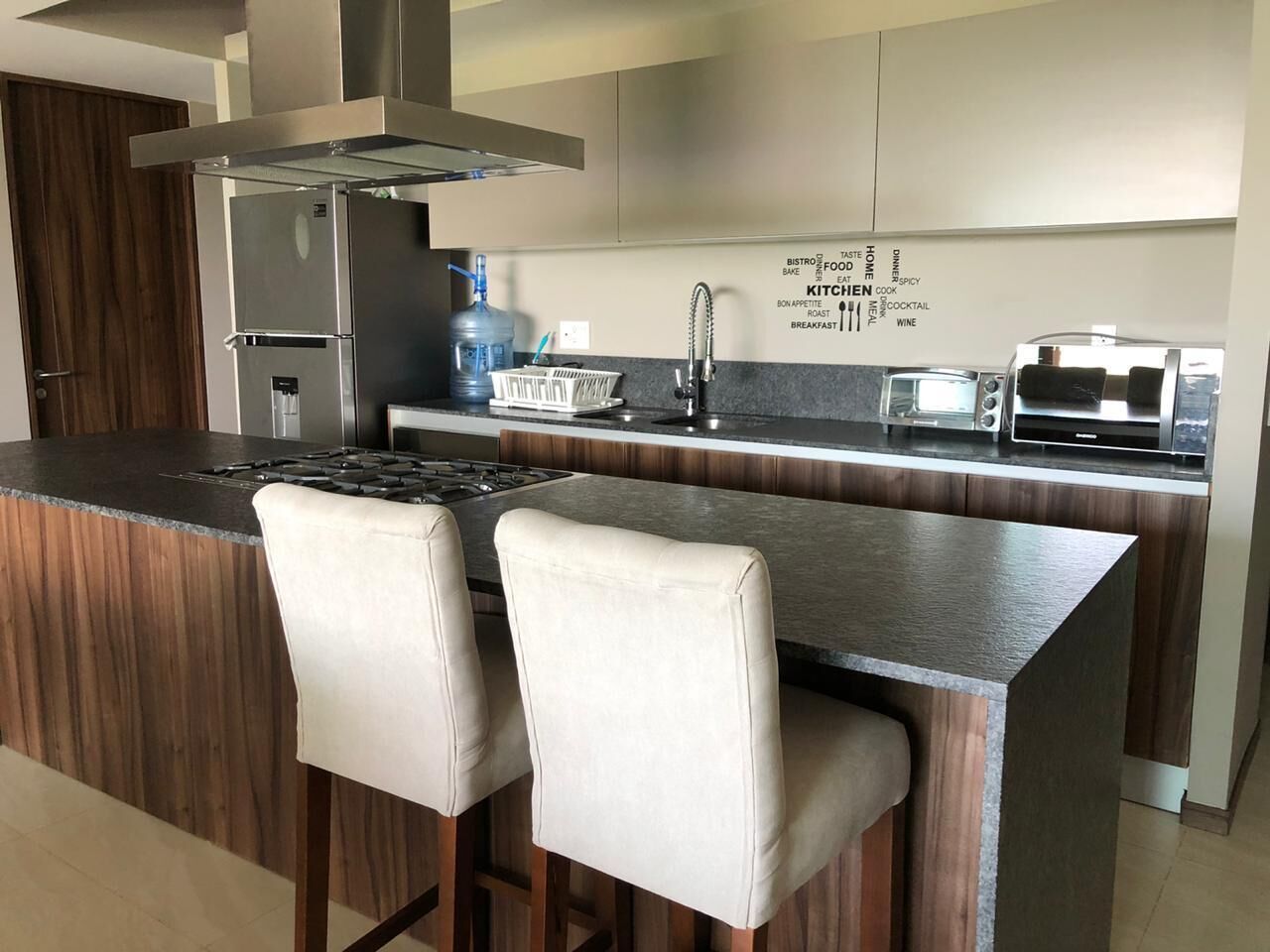 A modern kitchen with a central island, stainless steel appliances, and a word cloud on the wall.