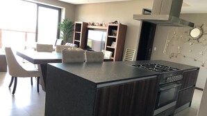 A modern kitchen with a central island, built-in oven, and a dining area with chairs and a table. - Luxury apartment in Acapulco diamond (Acapulco de Juárez)
