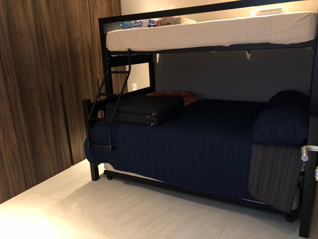 Een stapelbed met een matras, kussens en een koffer.
