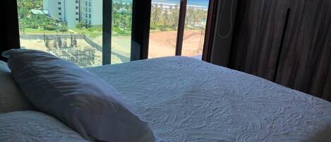 Habitación de hotel con una cama grande, vista a una playa y un edificio al fondo.