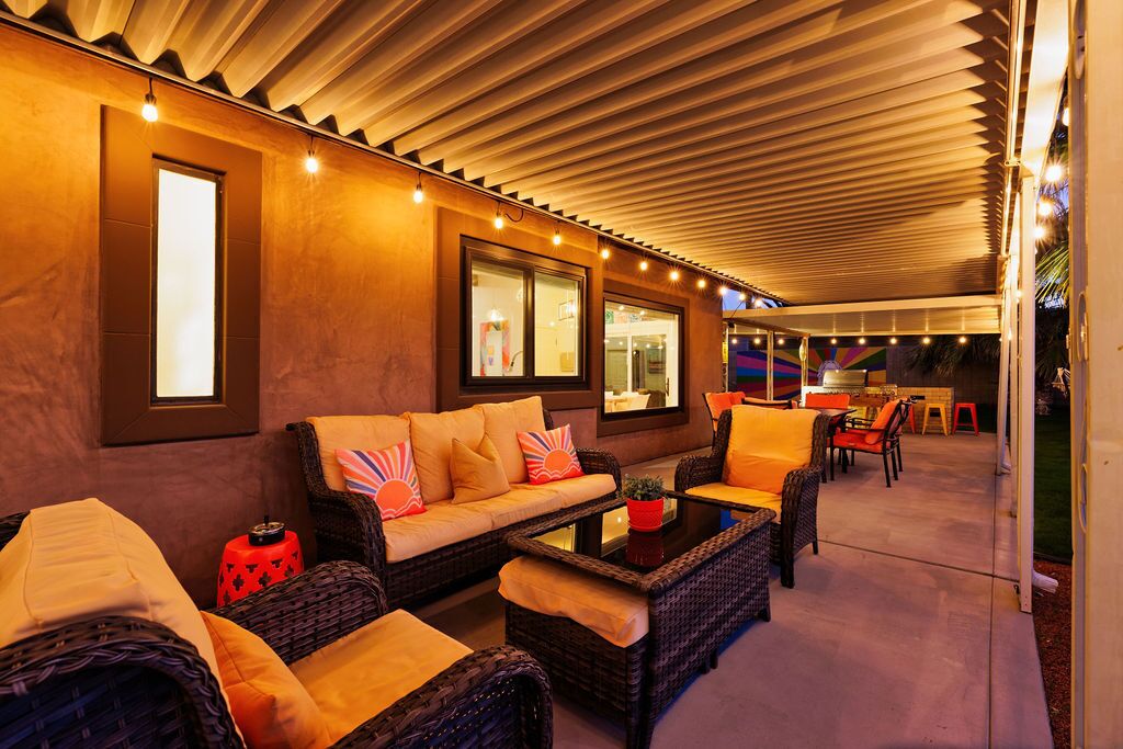 An outdoor lounge area with wicker furniture, a glass table, and a ceiling with wooden slats.